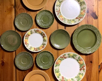 May include: A collection of 10 green and yellow ceramic plates with various floral and fruit designs. The plates are arranged on a wooden surface.