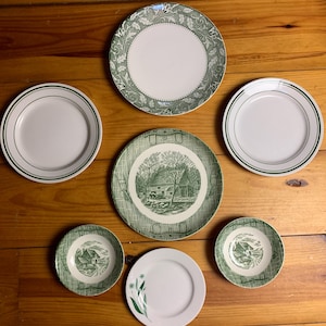 May include: Set of six green and white ceramic plates with various designs. The plates feature a farmhouse scene, a floral design, and a simple border.