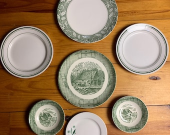 May include: Set of six green and white ceramic plates with various designs. The plates feature a farmhouse scene, a floral design, and a simple border.