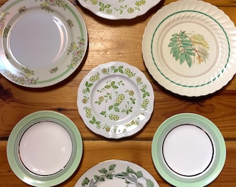 May include: Seven decorative plates with green and white floral patterns. The plates are arranged in a circle on a wooden surface.