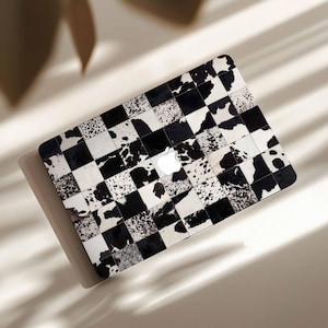 May include: A laptop skin featuring a black and white cowhide pattern in a checkerboard design. The skin has a white Apple logo in the center. The design is a mix of solid black, white, and speckled patches.