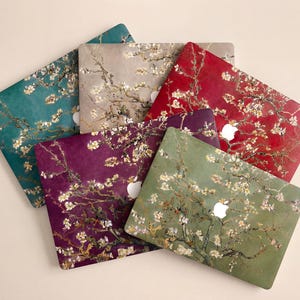 May include: A collection of laptop cases featuring a floral design in various colors. The cases showcase a painting of blossoming branches in shades of teal, beige, red, purple, and green. Each case has a white apple logo.