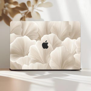 May include: A laptop with a floral design. The cover features a pattern of overlapping, light beige, petal-like shapes. The Apple logo is visible in black. The laptop is on a white surface.