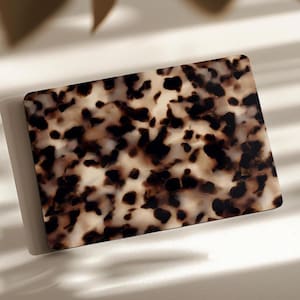 Può includere: Una carta rettangolare caratterizzata da un classico motivo tartarugato con un mix di macchie traslucide marrone scuro, nere e color crema. La superficie è liscia e lucida, mostrando un design maculato organico e irregolare su tutto il pezzo.