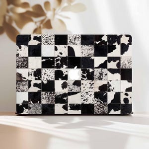 May include: A black and white checkered laptop case with a cowhide pattern. The case features a patchwork design with squares of black and white cowhide. The Apple logo is visible in the center of the case.