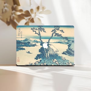 Può includere: Una custodia per laptop con una stampa di paesaggio giapponese. Il design presenta una scena tradizionale con una piccola capanna, alberi e acqua, in tonalità blu, beige e bianco. Il logo Apple è visibile.