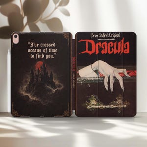 May include: A tablet case featuring a Dracula theme with a dark castle and the text I've crossed oceans of time to find you on the left panel. The right panel displays the title Dracula in red with a pale hand resting on a coffin lid.