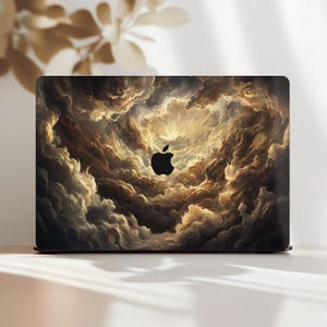 Op de afbeelding: Laptop skin met een dramatisch wolkenlandschap ontwerp in tinten bruin, goud en wit. Het Apple-logo is zwart. Het ontwerp bedekt het gehele bovenoppervlak van de laptop.