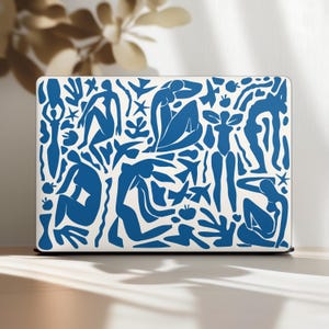 May include: A white laptop case featuring a blue abstract design with human figures, stars, and floral shapes. The design is reminiscent of Matisse's cut-outs. The case is rectangular and sits on a light-colored surface.