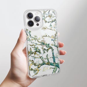 Puede incluir: Funda transparente para teléfono con una pintura de una rama de árbol en flor. El diseño presenta flores blancas y ramas verdes y marrones. La funda se sostiene en una mano y tiene un borde transparente.