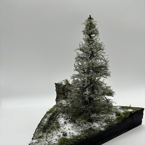 May include: A miniature winter scene featuring a snow-covered evergreen tree on a triangular base covered in green moss and white snow.