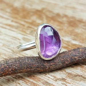 Op de afbeelding: Een zilveren ring met een paarse amethist edelsteen. De ring heeft een unieke, onregelmatige vorm en een gladde, gepolijste afwerking.