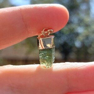 May include: A green gemstone pendant with a silver setting. The pendant is shaped like a long, thin crystal.