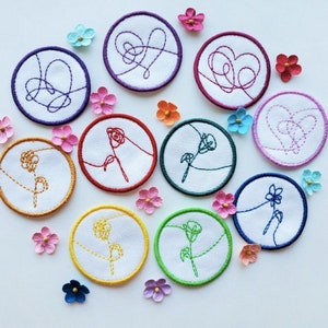 May include: Ten embroidered iron-on patches with various designs, including hearts, flowers, and abstract shapes. The patches are on a white background with small pink, purple, and blue flowers scattered around them.