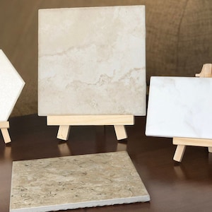 May include: Four ceramic tiles displayed on small wooden easels. The tiles are in various shapes and sizes, and have different patterns and colors. The tiles are on a dark brown wooden surface.