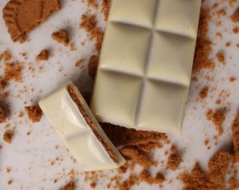 May include: A broken white chocolate bar with a layer of cookie crumbs on top. The chocolate bar is broken into two pieces, one of which is lying on its side. There are cookie crumbs scattered around the chocolate bar.