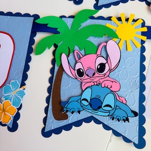 Puede incluir: Una pancarta azul con borde festoneado presenta un tema tropical. Incluye una palmera, un sol amarillo y los personajes de dibujos animados Stitch y Angel. La pancarta tiene un fondo texturizado con motivos florales.