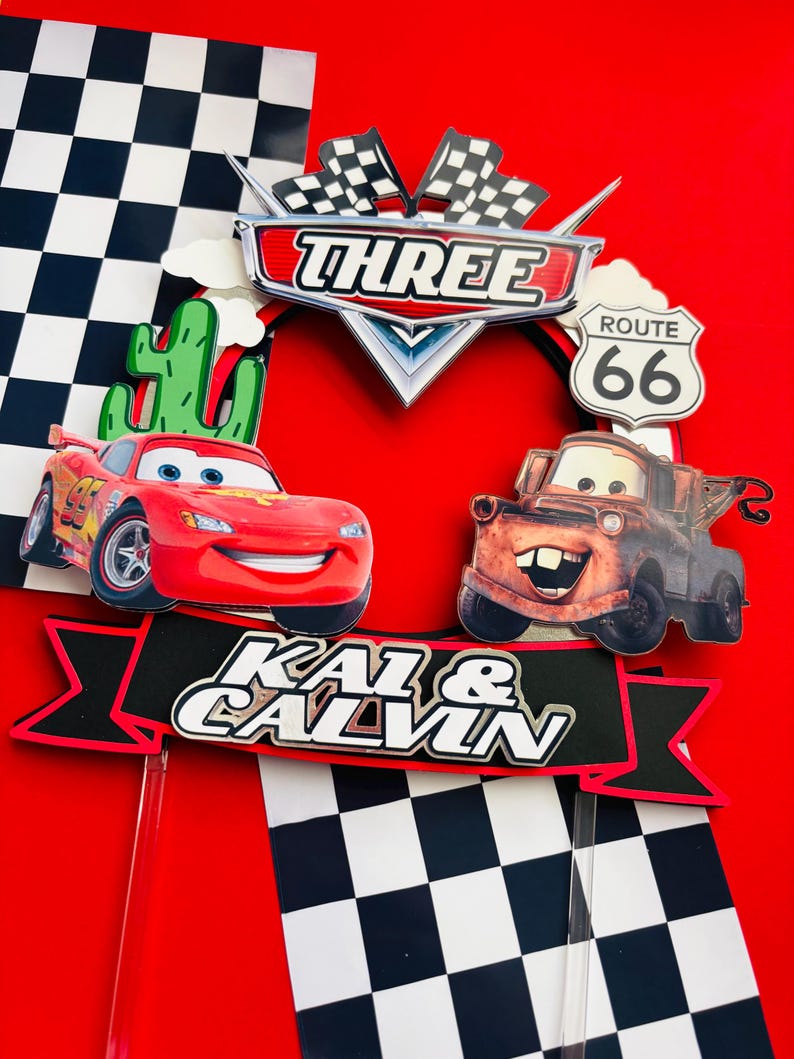 May include: A red and black cake topper with a checkered flag design, featuring the characters Lightning McQueen and Mater from the Disney Pixar Cars movie. The topper also includes a banner with the text "Kai & Calvin" and a sign that says "Three" and "Route 66".