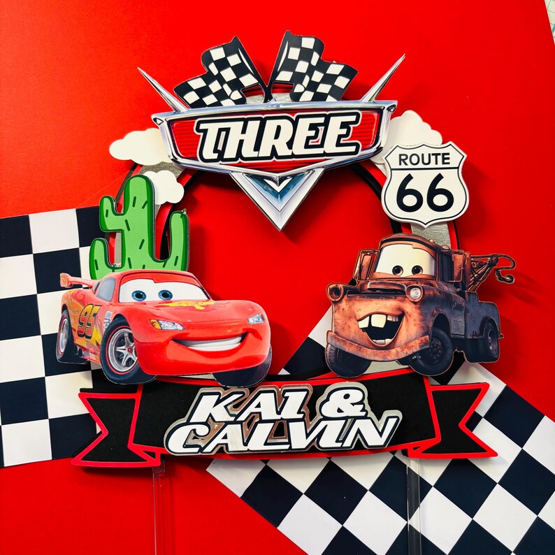 May include: Red and black cake topper featuring Lightning McQueen and Mater from the Cars movie. The topper also includes a checkered flag, a cactus, and a Route 66 sign. The text "Three" and "Kai & Calvin" are also included.