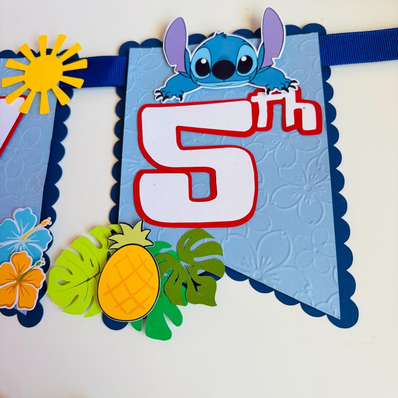 Puede incluir: Una pancarta azul con borde festoneado, con el n&uacute;mero "5" en blanco con un contorno rojo. Tambi&eacute;n hay un personaje de dibujos animados y decoraciones tropicales, incluyendo una pi&ntilde;a y hojas. Se ve un sol amarillo.
