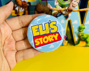 以下が含まれることがあります： 「ELI'S STORY」と書かれた青と黄色のボタン。ボタンはトイストーリーをテーマにしたパーティーの装飾を背景にしている。