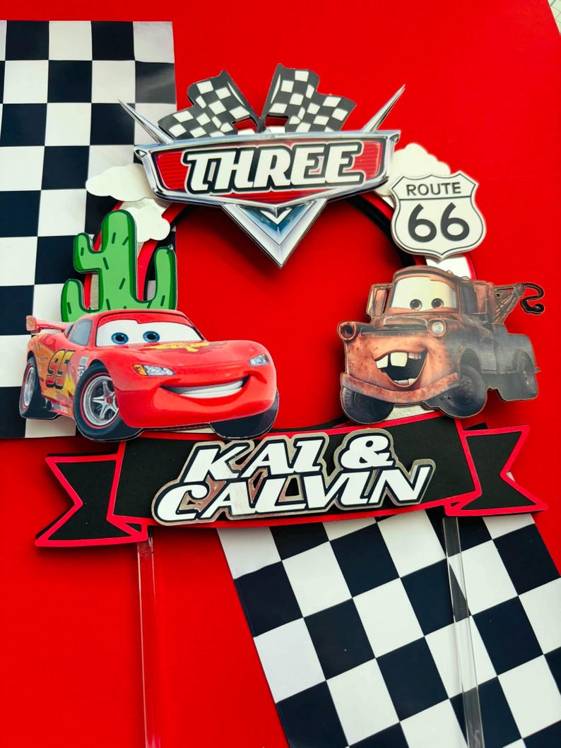 May include: Red and brown Cars themed cake toppers with a checkered flag background. The toppers feature Lightning McQueen and Mater from the Disney Pixar movie Cars. The toppers also include a sign that says "Three" and "Route 66". The toppers are on sticks and are ready to be placed on a cake.