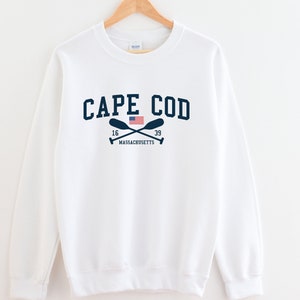 May include: White sweatshirt with a navy blue graphic that says "CAPE COD" with a small American flag and crossed oars. The text "16 MASSACHUSETTS 39" is below the graphic.