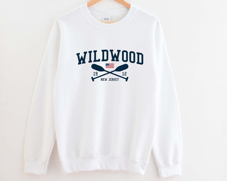 May include: White sweatshirt with a navy blue graphic print of the text "WILDWOOD" with a crossed paddle design and a small American flag. The text "19 12 NEW JERSEY" is printed below the graphic.