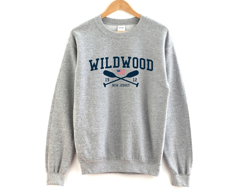 May include: A gray sweatshirt with the text "WILDWOOD" in navy blue lettering. The text is surrounded by two crossed oars with an American flag in the center. The text "19" and "12" are on either side of the oars. The text "NEW JERSEY" is below the oars.