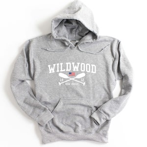 Pu&ograve; includere: Una felpa con cappuccio grigia con una stampa grafica bianca che dice "WILDWOOD" con una piccola bandiera americana e remi incrociati sotto. Il testo "1912 NEW JERSEY" &egrave; stampato sotto i remi.