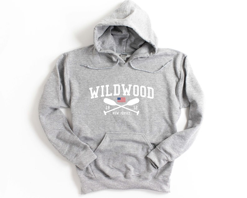 Pu&ograve; includere: Una felpa con cappuccio grigia con una stampa grafica bianca che dice "WILDWOOD" con una piccola bandiera americana e remi incrociati sotto. Il testo "1912 NEW JERSEY" &egrave; stampato sotto i remi.