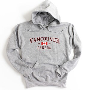 May include: A gray hooded sweatshirt with a red and white Canadian flag and the text "Vancouver 18 86 Canada" printed on the front.