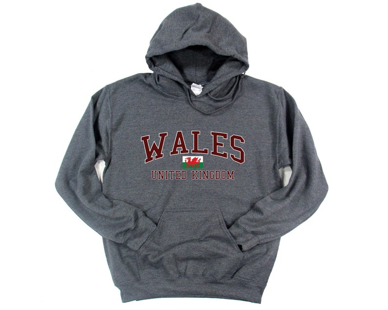 Puede incluir: Una sudadera con capucha gris oscuro con la palabra "WALES" en letras marrones y la bandera galesa debajo. El texto "UNITED KINGDOM" est&aacute; impreso en marr&oacute;n debajo de la bandera.