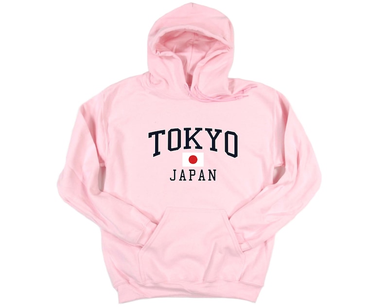 Peut inclure: Un sweat &agrave; capuche rose clair avec une poche avant et une capuche. Le mot "TOKYO" est imprim&eacute; en lettres majuscules bleu marine au-dessus du mot "JAPAN" en noir, avec un drapeau japonais entre les deux. Le sweat &agrave; capuche est en mati&egrave;re douce.