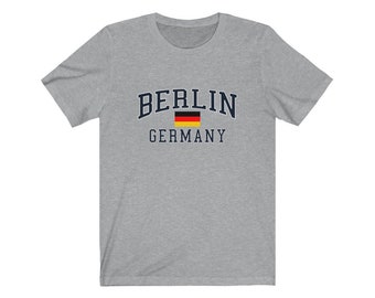 May include: A heather gray t-shirt with a navy blue print that says "BERLIN GERMANY" with a small German flag.