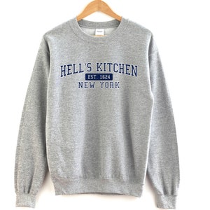May include: A grey sweatshirt with the text "HELL'S KITCHEN EST. 1624 NEW YORK" printed in navy blue.