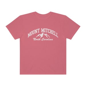 May include: A pink t-shirt with a white graphic of a mountain range and the text "MOUNT MITCHELL North Carolina".