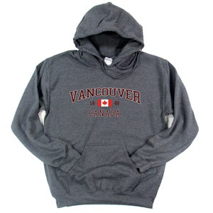 May include: A dark gray hooded sweatshirt with a maroon print that says "Vancouver 1886 Canada" with a Canadian flag in the middle.