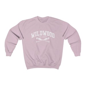 May include: A light pink sweatshirt with the text "WILDWOOD NEW JERSEY" in white with a graphic of two crossed oars.