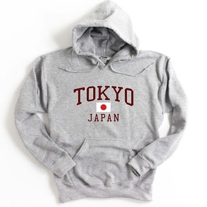 Peut inclure: Un sweat &agrave; capuche gris clair avec une poche avant. Le mot "TOKYO" est imprim&eacute; en lettres majuscules bordeaux au-dessus du mot "JAPAN" et d'un drapeau japonais. Le sweat-shirt a une capuche &agrave; cordon.