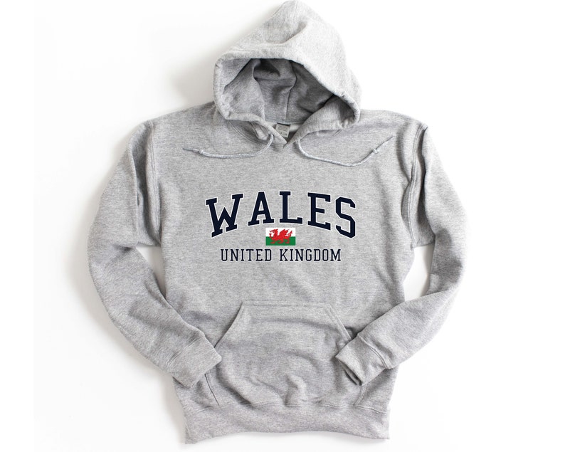 Puede incluir: Sudadera gris con capucha con la palabra "WALES" en letras azul marino y la bandera galesa debajo. El texto "UNITED KINGDOM" est&aacute; impreso debajo de la bandera.