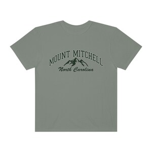May include: A light gray t-shirt with a green graphic of mountains and the text "MOUNT MITCHELL North Carolina".