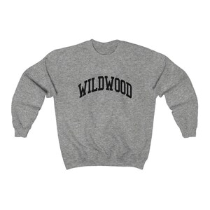 May include: A heather gray sweatshirt with the word "WILDWOOD" arched across the chest in black block letters. The sweatshirt has long sleeves and a crew neck. The fabric appears to be a soft, comfortable material.