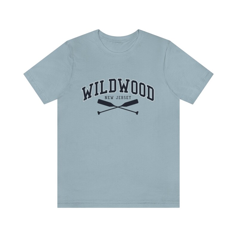 May include: A light blue t-shirt with a navy blue graphic of the text "WILDWOOD NEW JERSEY" in a collegiate font with two crossed oars underneath.