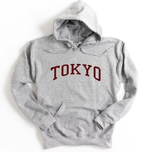 May include: A gray hooded sweatshirt with a maroon "TOKYO" graphic on the front.