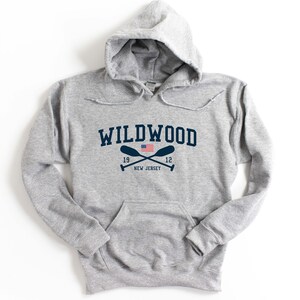 Pu&ograve; includere: Felpa con cappuccio grigia con una grafica blu navy del testo "WILDWOOD" con una piccola bandiera americana e remi incrociati sotto. Il testo "19 12 NEW JERSEY" &egrave; sotto i remi.