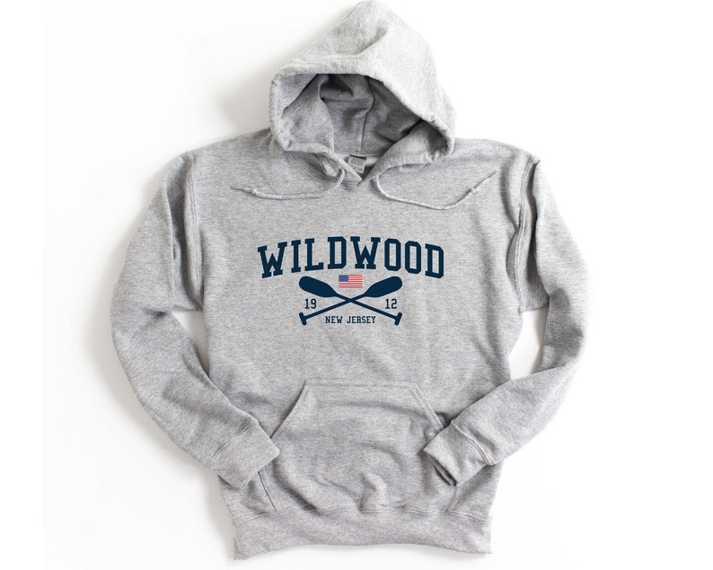 Pu&ograve; includere: Felpa con cappuccio grigia con una grafica blu navy del testo "WILDWOOD" con una piccola bandiera americana e remi incrociati sotto. Il testo "19 12 NEW JERSEY" &egrave; sotto i remi.