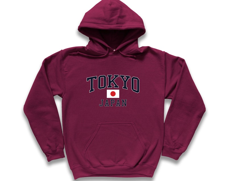 Peut inclure: Un sweat &agrave; capuche bordeaux avec le mot "TOKYO" en lettres blanches avec un contour bleu marine. En dessous du mot "TOKYO" se trouve le mot "JAPAN" et un petit drapeau japonais. Le sweat-shirt a une poche avant.