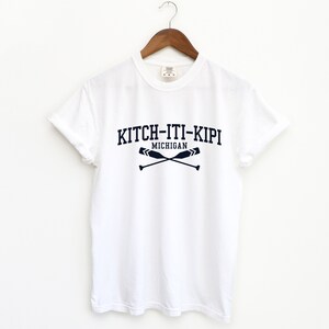 May include: White t-shirt with a navy blue graphic print that says "KITCH-ITI-KIPI MICHIGAN" with two crossed oars.