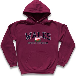 Puede incluir: Sudadera con capucha color burdeos con el texto "WALES UNITED KINGDOM" y un peque&ntilde;o gr&aacute;fico de la bandera galesa.